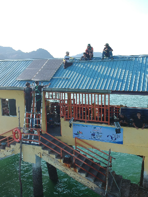 Technologists install solar panels on a roof of a building built over water.